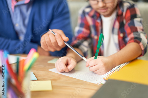 Close up of hands of middle aged latin father helping his son, school child with homework while sitting together at the desk at home