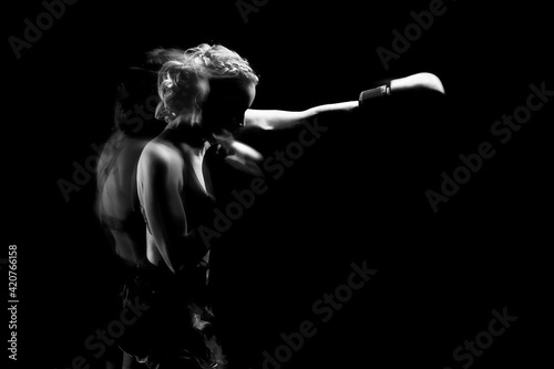 Young woman goes in for sports. She trains with boxing gloves. The photo is black and white..Movement and blow.