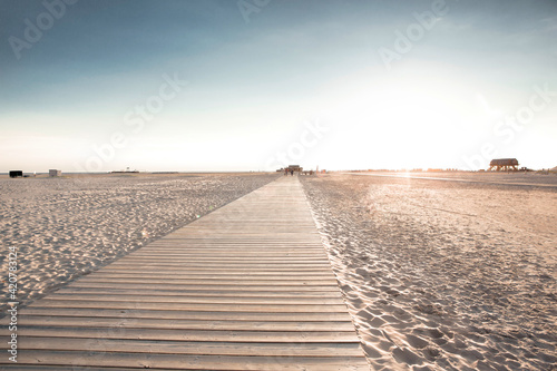 Wooden boardwalk on sandy beach. Many footprints in sand after rush summer day on seaside.