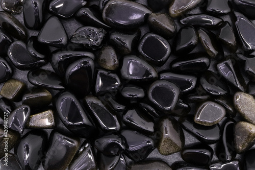 Gold obsidian jewel heap on light wood texture. Pile mineral pebbles background.