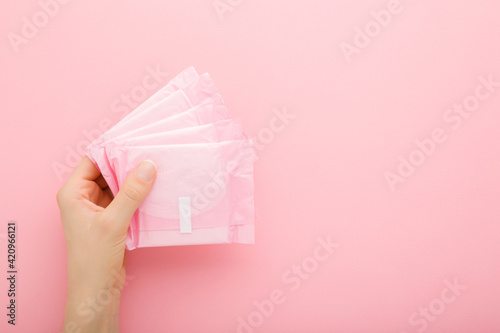 Young adult woman hand holding packs of sanitary towel on light pink table background. Pastel color. Closeup. Empty place for text. Top down view.
