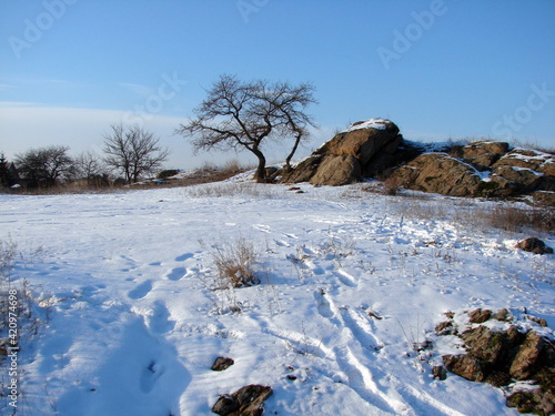 Landscape of snow-covered Dnieper mounds under the rays of the evening sun against a clear frosty blue sky.