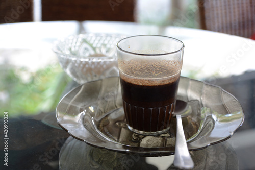 インドネシアのバリ島、ウブドのカフェ。ガラスのグラスのブラックコーヒー&ソーサー。ガラステーブル。