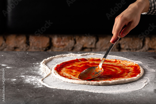 Making a pizza spreding tomato sauce on the dough on the grey concrete background