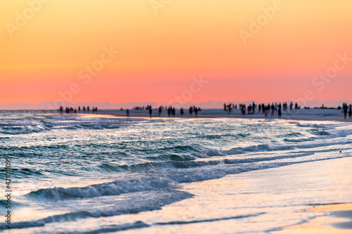 Siesta Key, Florida near Sarasota, USA at colorful sunset with coast gulf of mexico, silhouette of distant people in far distance on beach, waves washing