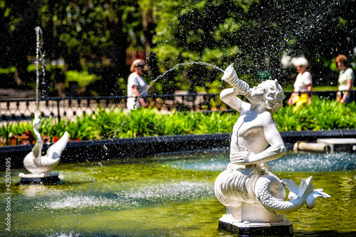 Water fountain in Forsyth park, Georgia with sculpture statues of white marble in Savannah, Georgia on sunny summer day with people in blurry blurred background