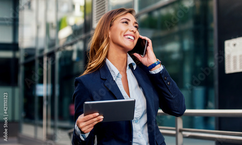 Businesswoman holding tablet and making a phone call in front of the corporation. Business, lifestyle concept