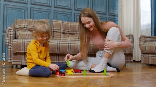 Mother with little daughter child girl riding toy train on wooden railway blocks board game at home