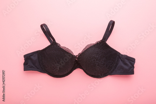 Black dark lace bra on light pink table background. Pastel color. Closeup. Daily female underwear. Top down view.