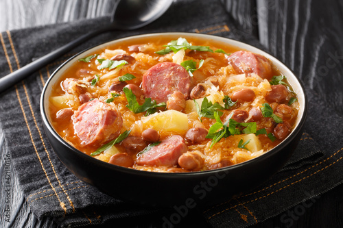 Homemade hot sauerkraut soup with borlotti beans, potatoes and sausages close-up in a bowl on the table. horizontal