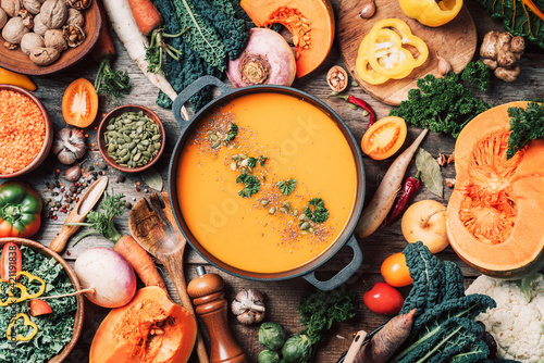 Pumpkin soup with vegetarian cooking ingredients, wooden spoons, kitchen utensils on wooden background. Top view. Vegan diet. Autumn harvest. Healthy, clean food and eating concept. Zero waste