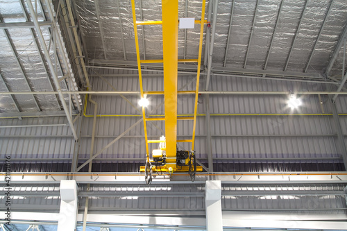 Overhead crane inside factory or warehouse. That industrial machinery or lifting equipment consist of hoist, hook and wire rope traveling on beam girder structure. For manufacturing production plant.