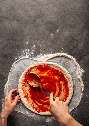 Making a pizza spreding tomato sauce on the dough on the grey concrete background