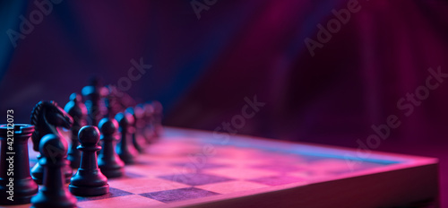 Chess pieces on a chessboard on a dark background shot in neon pink-blue colors. The figure of a chess .Close up.