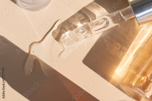 close up of pipette with pouring liquid serum with golden bottle and shadows