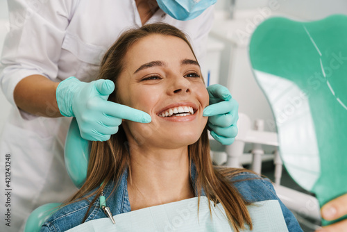 European young woman smiling while looking at mirror in dental clinic