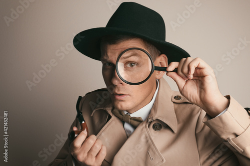 Male detective with smoking pipe looking through magnifying glass on beige background