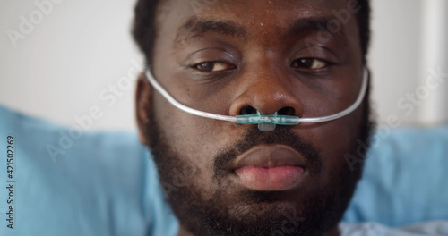 Close up of young african man patient with nasal cannula resting in bed at hospital