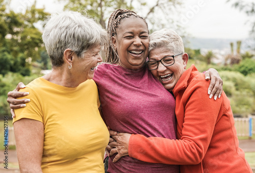 Happy multiracial senior women having fun together outdoor - Elderly generation people hugging each other at park