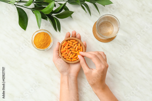 Female hands with turmeric pills on light background