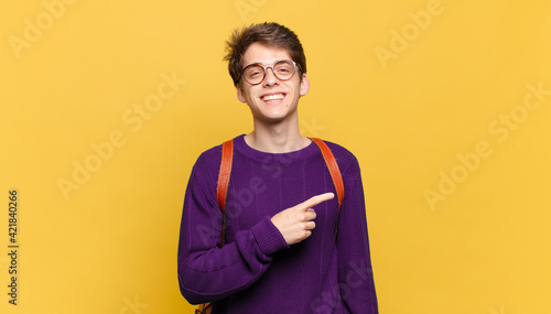 young student boy smiling cheerfully, feeling happy and pointing to the side and upwards, showing object in copy space