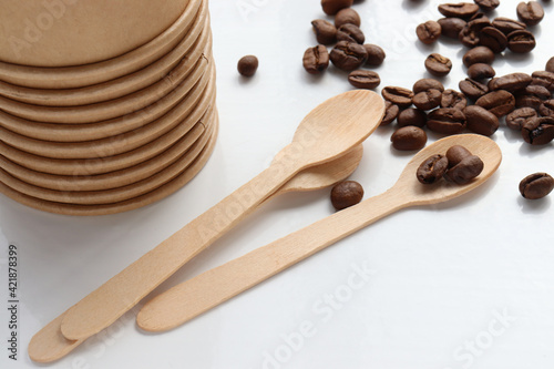 Flat lay composition with coffee beans, kraft paper cup and wooden spoon. Top view, copy space