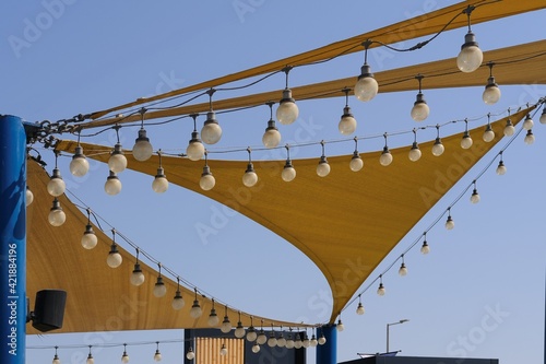 Dynamic texture of fabric stretch roof made of canvas sail with rows of bulb lamps for party night lighting on blue sky background.