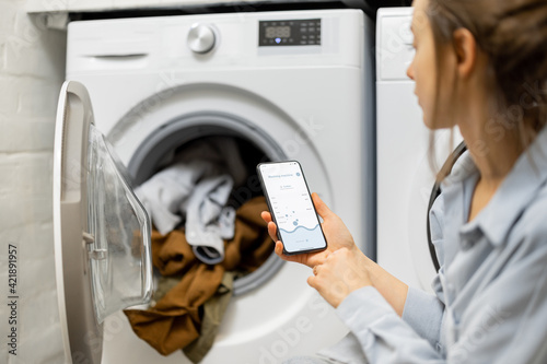 Woman controls washing machine with a smartphone