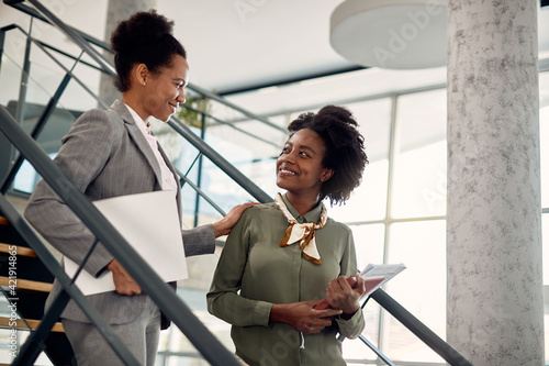 Happy black businesswoman talks to female mentor who leads her through office building.
