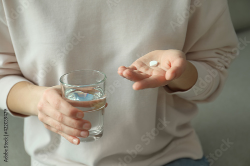 Young woman with abortion pill and glass of water on sofa, closeup