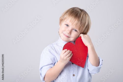 Cute Caucasian child is tenderly holding toy red heart on white background. Eye contact. Studio light. Concept of childhood, love, mother's day, health care, valentine. Horizontal. Copy space.