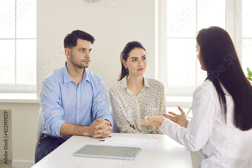 Doctor counseling millennial family couple with health problems about medical treatment at clinic. Female practitioner explaining diagnosis giving prescription providing advice for infertility cure