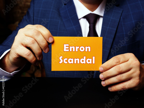 Blank orange business card in a hand with phrase Enron Scandal . Horizontal shot. Close-up