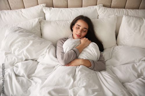 Beautiful young woman wrapped with soft blanket sleeping in bed at home, above view