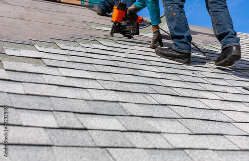 roofer installing roof shingles with nail gun