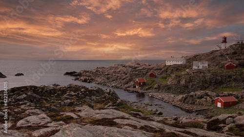 landscape rocky coast of the northern sea, traditional wooden red Norwegian houses and the southern lighthouse Lindesnes fyr Norway in the spring evening