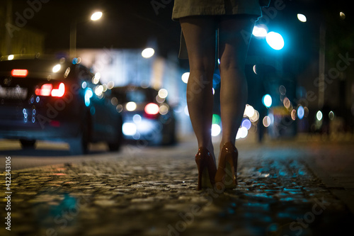 Shapely female legs in high heels on the street against the background of the lights of moving cars.