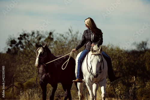 Western lifestyle shows woman riding horse bareback while ponying mare through Texas field.