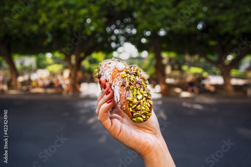 Female hand holding a pistachio cannoli in front of a park