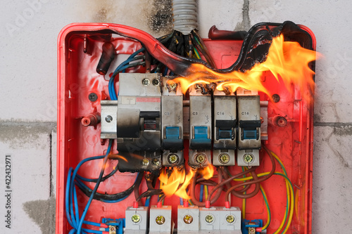 Burning switchboard from overload or short circuit on wall close-up. Circuit breakers on fire from overheating due to poor connection or poor quality wires. Faulty home wiring concept