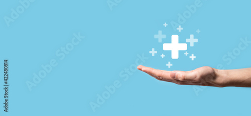 Male hand holding plus icon on blue background. Plus sign virtual means to offer positive thing (like benefits, personal development, social network)Profit,health insurance, growth concepts