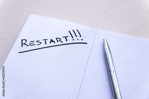 Restart! Starting again after a break, after a pandemic. Word "Restart" written in black ink on a blank page of a notebook, placed on a wooden surface. 