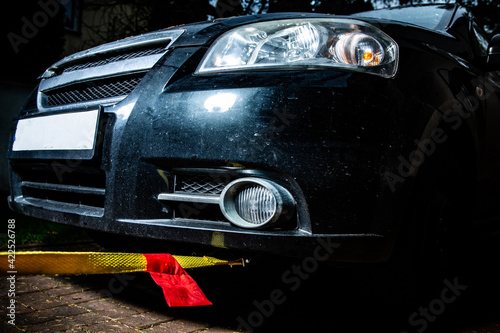 A horizontal view of a black automobile with yellow towline attached to a car towing eyelet. Towing a broken vehicle with a tow rope at night. Car assistance services.