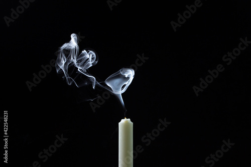 Smoke from a candle on a black background. An extinguished candle on a dark background. White smoke