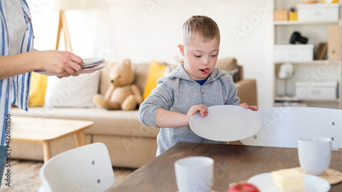 Unrecognizable single mother setting table for breakfast with down syndrome son at home.