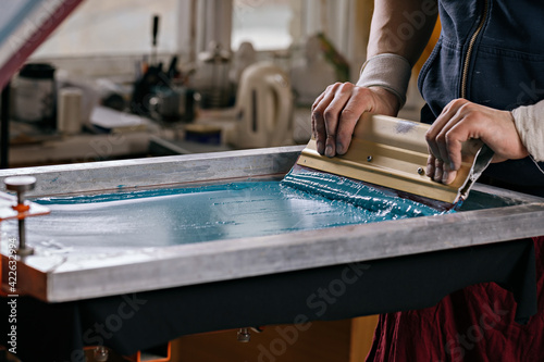 selective focus photo of male hands with squeegee. serigraphy production. printing images on t-shirts by silkscreen method in a design studio