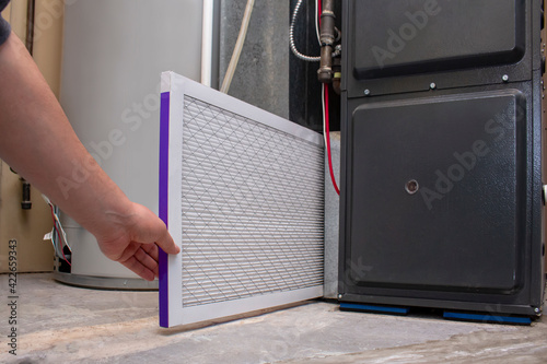 A person changing an clean air filter on a high efficiency furnace