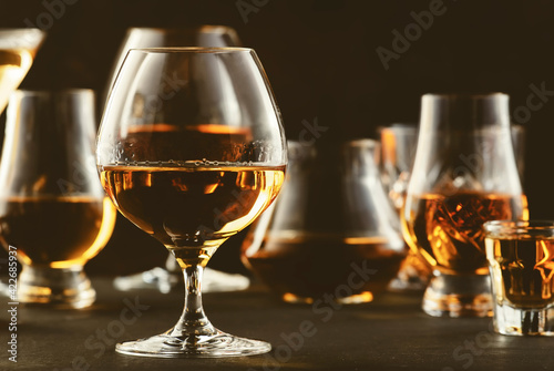 Hard strong alcoholic drinks and distillates in glasses in assortment: vodka, cognac, tequila, scotch, brandy and whiskey, grappa, liqueur, vermouth, tincture, rum. Brown background