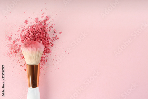 Makeup brush and scattered blush on pink background, top view. Space for text