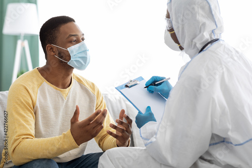 Doctor in PPE suit taking anamnesis for sick male patient